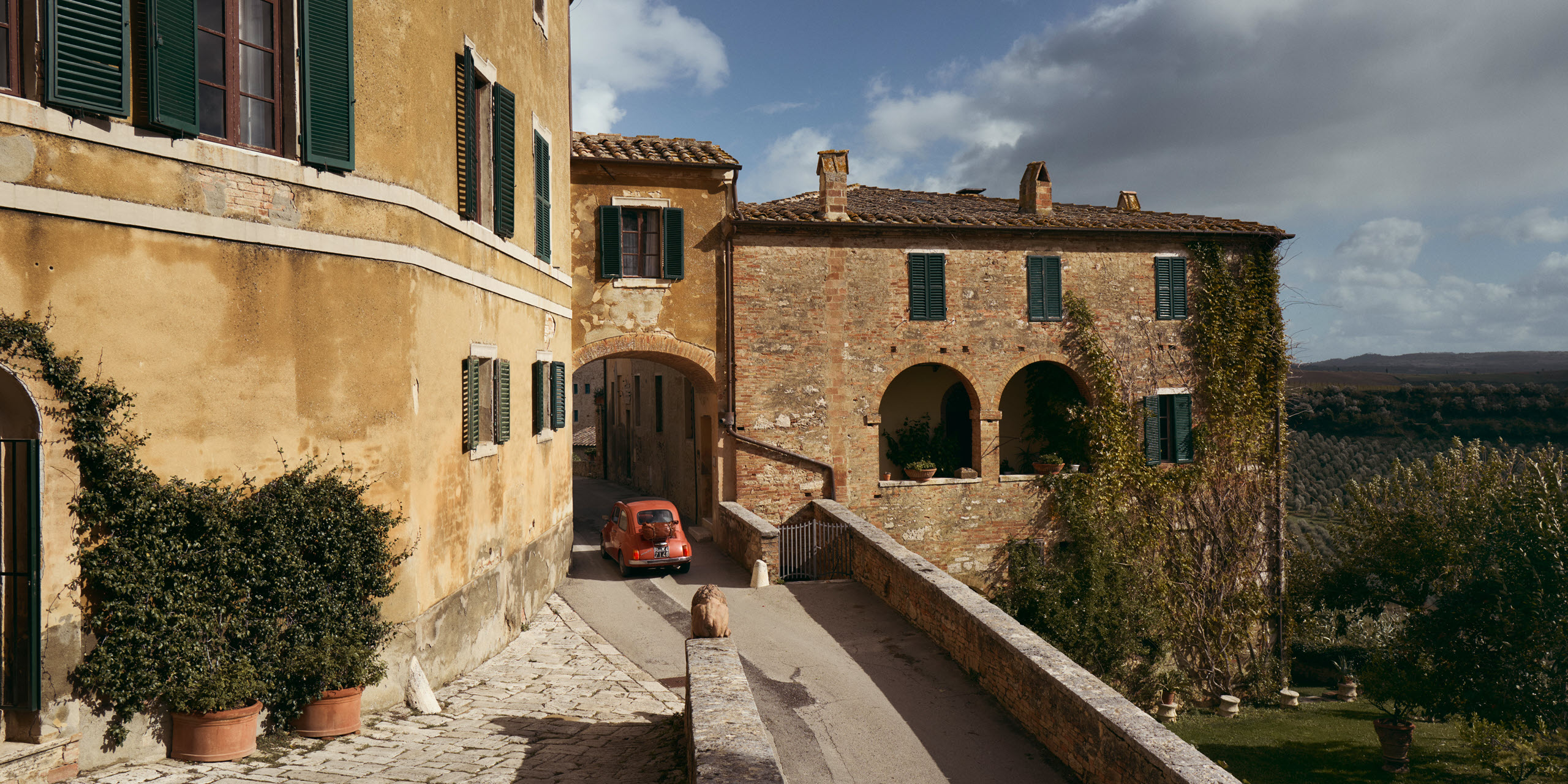 A small car driving through an archway on a narrow road in a village in Tuscany.