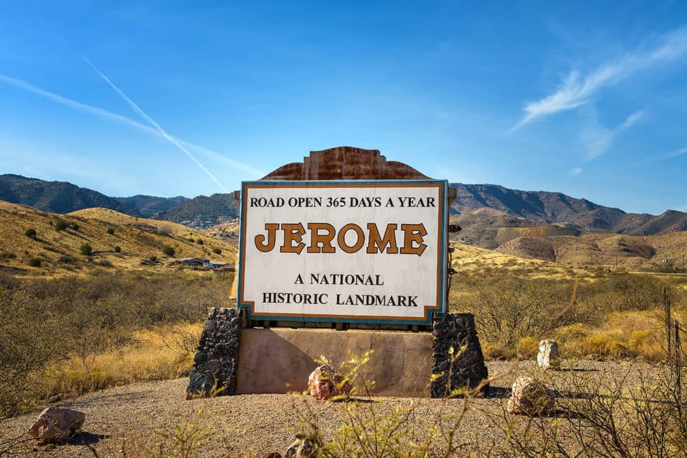 Historic city sign for Jerome, Arizona against the backdrop of mountains and blue skies.