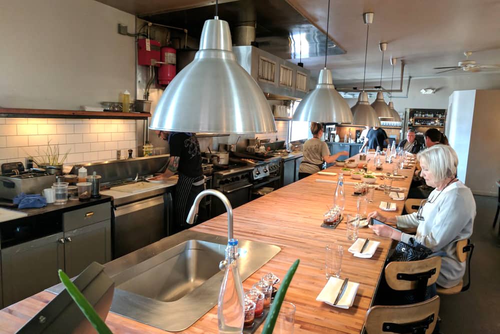 Diners at a wooden table facing the open kitchen at Revel, a well-lit, open-concept date restaurant in Seattle