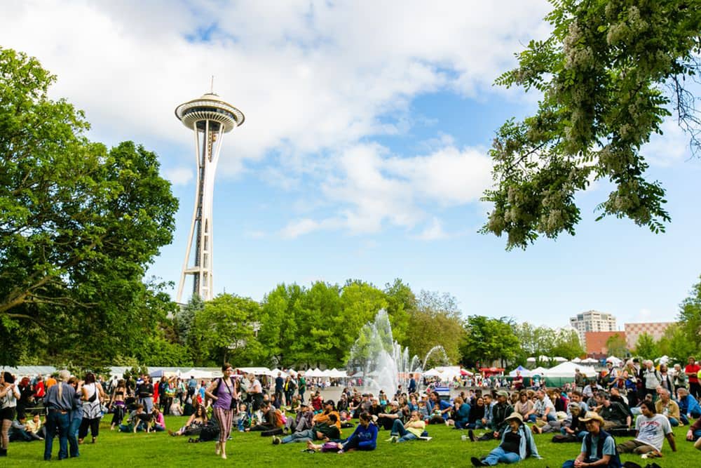 A group of people gathered at Seattle Center near International Fountain for a festival, a fun cheap date night in Seattle. The Space Needle stands in the background.