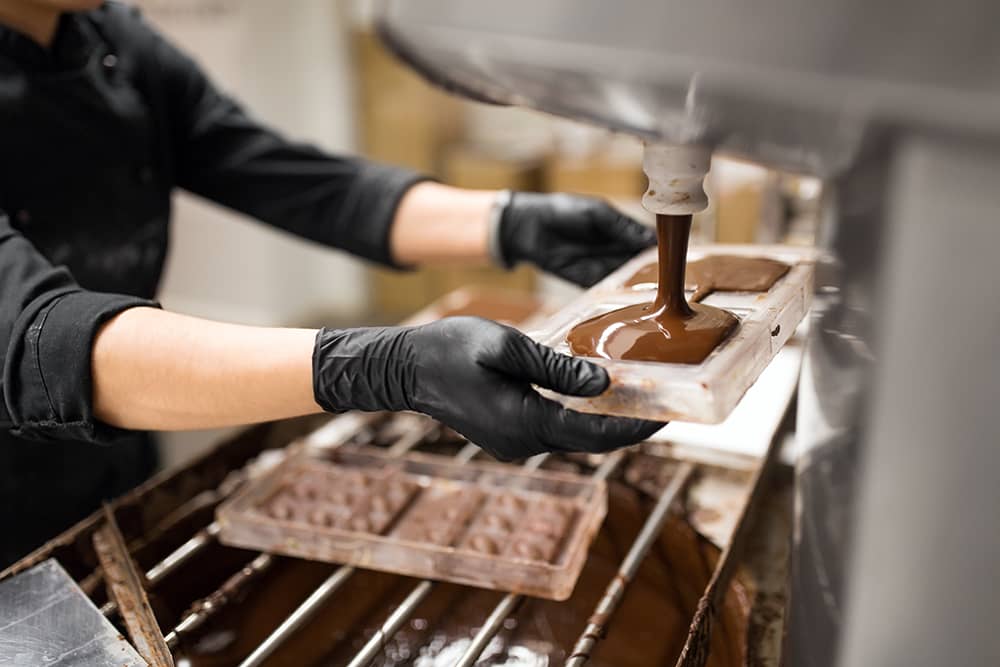 A view of hands moving chocolate along an assembly line, which you may see on the Hammond's Candy Factory tour, a free Denver activity.