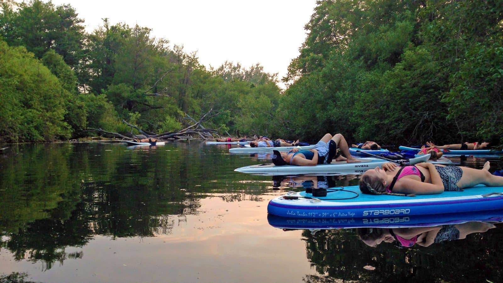 A group of people doing corpse pose while practicing yoga outdoors on stand-up paddle boards in Toronto