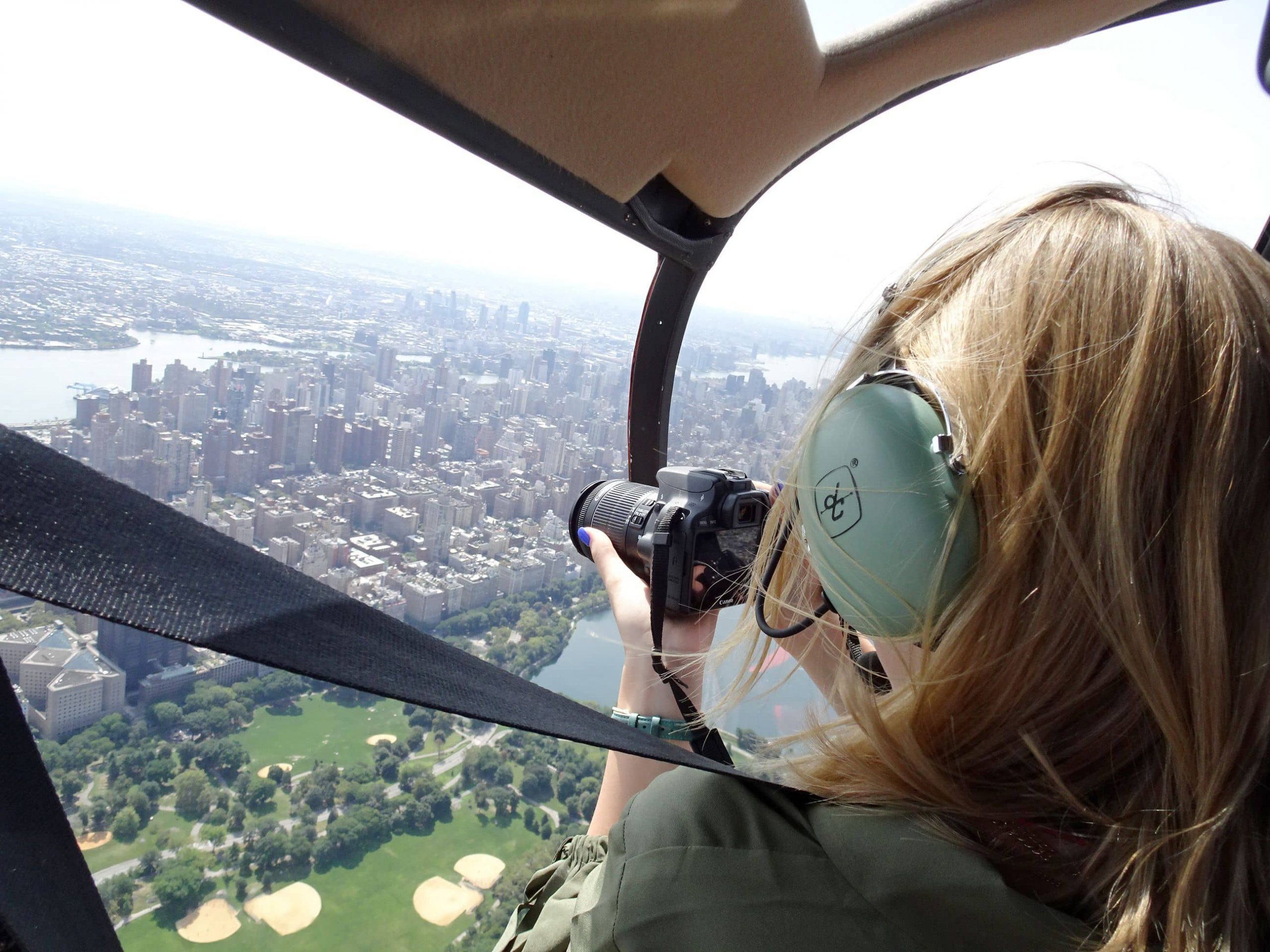 A woman in a helicopter photographing New York city from above with a large camera to take amazing travel photos