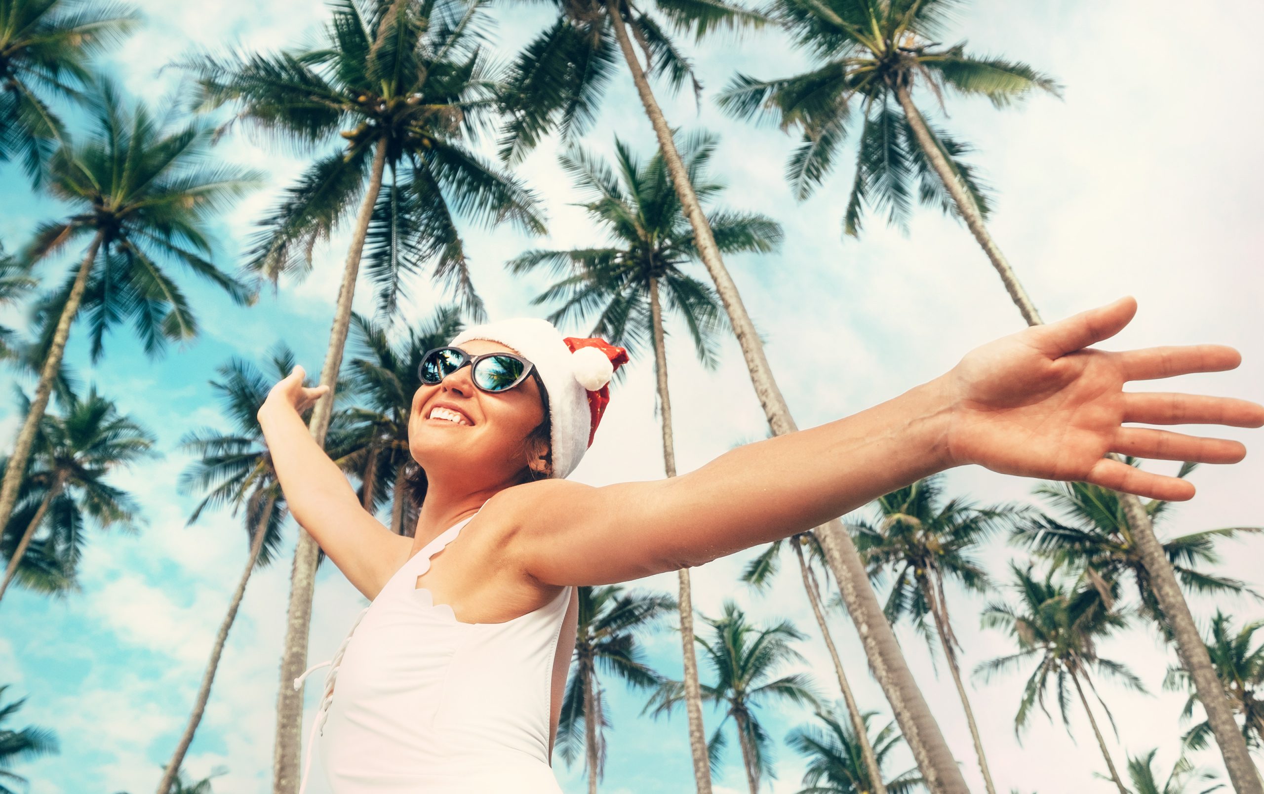 Girl with sunglasses and a Santa hat in front of palm trees