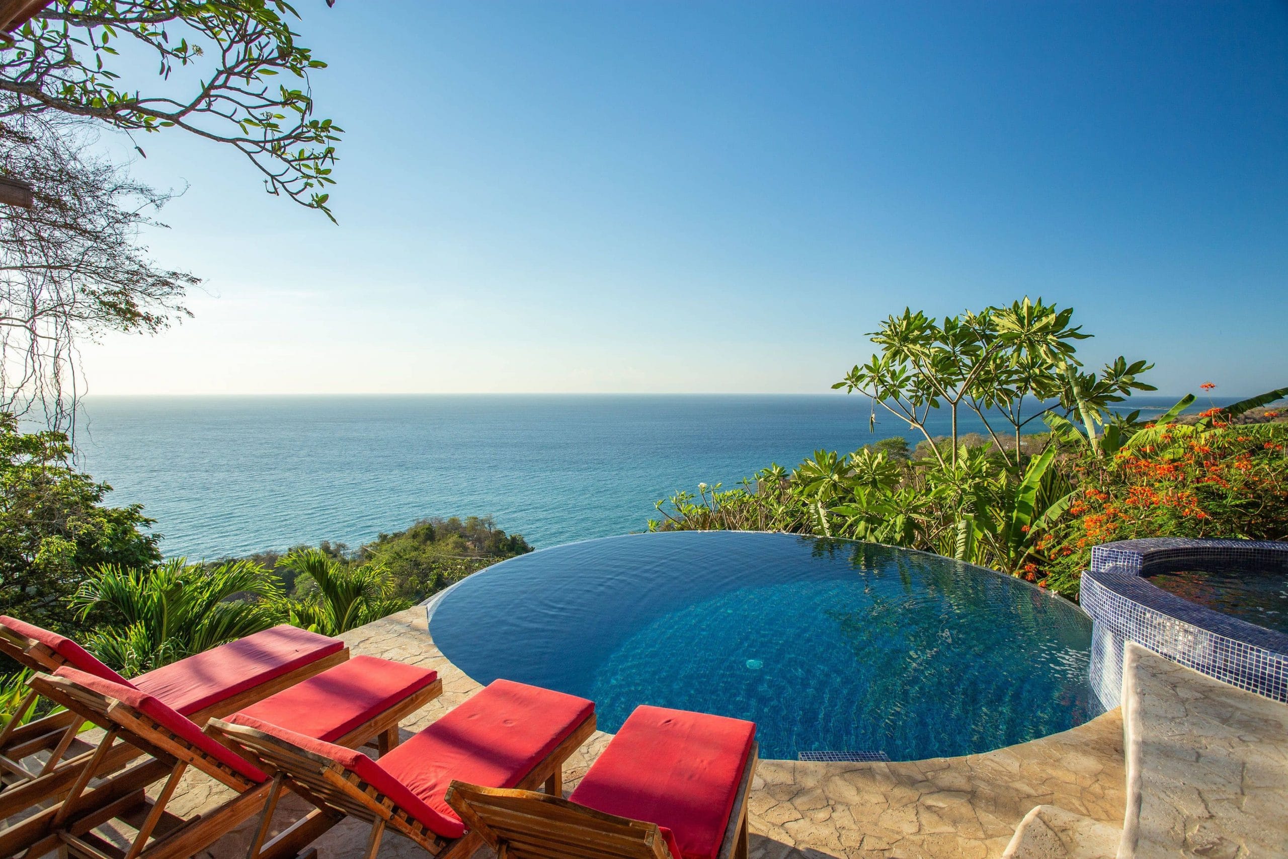 A pool side hot tub at the Anamaya Yoga Retreat in Costa Rica with vivid blue ocean waters in the distance and a jungle canopy view from red sun loungers for guests.