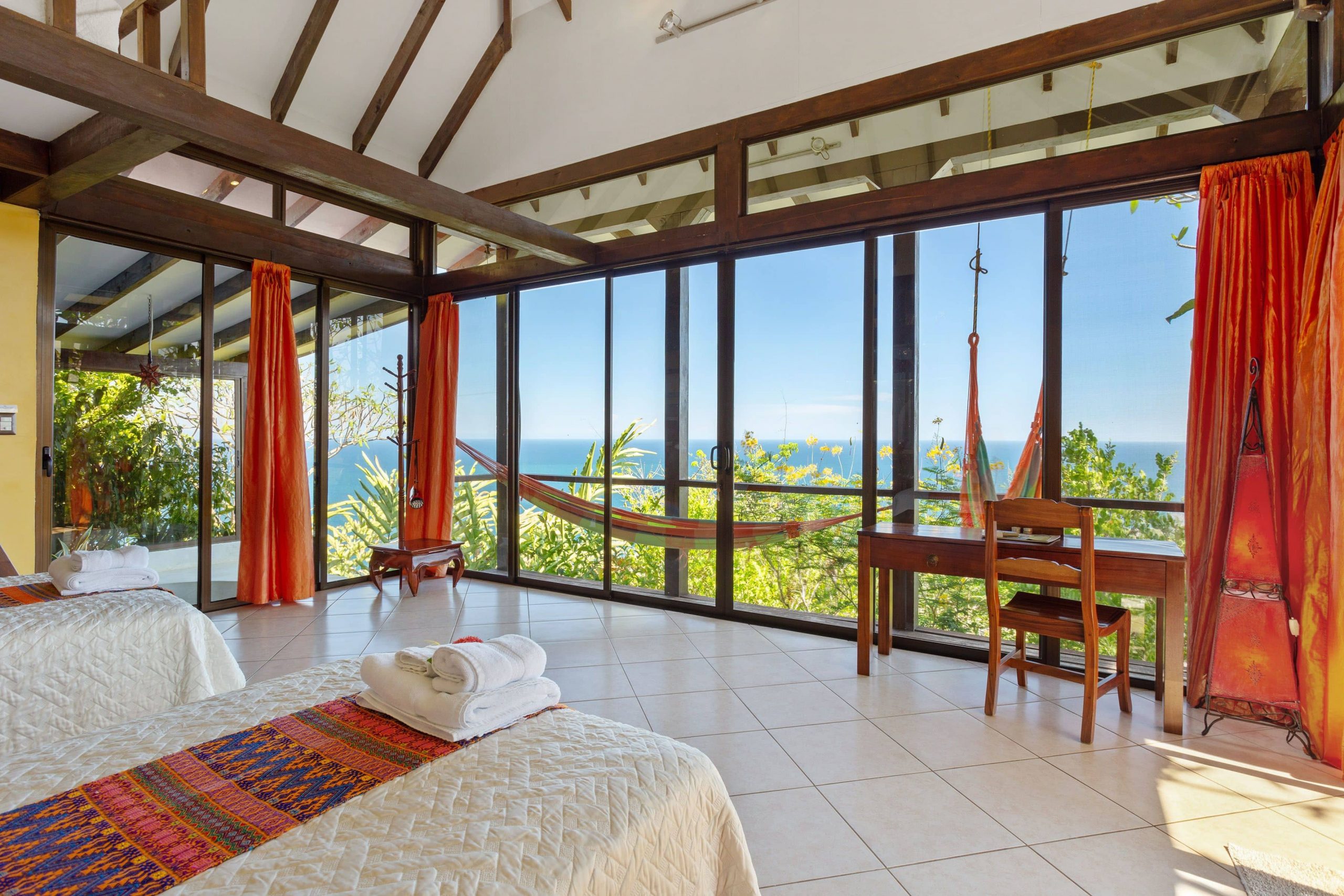 Inside one of the villas offered to guests of the Anamaya Yoga Retreat in Costa Rica with a hammock to relax, a desk with a view, white linens, and beautiful interior decor.