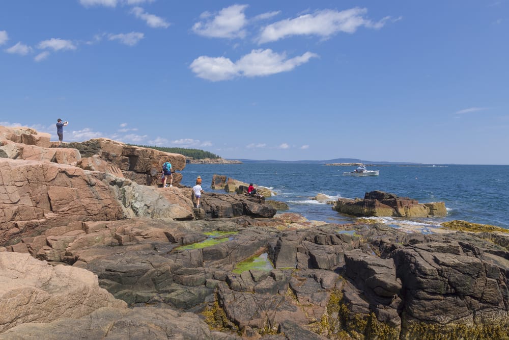 People walking on rocks by the sea at Arcadia National Park