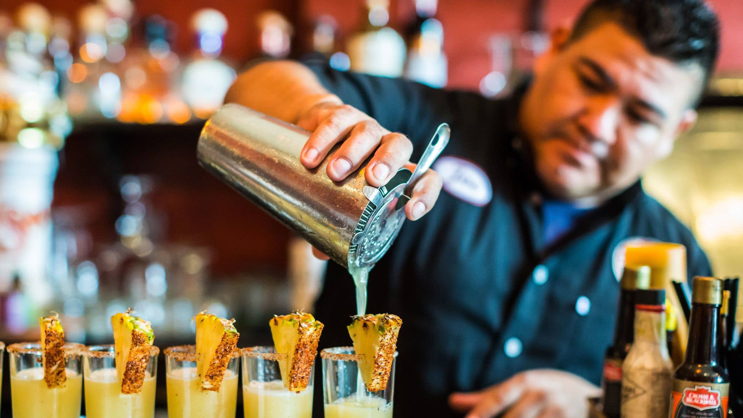 Bartender pouring a line of fruity mixed drinks in Mexico