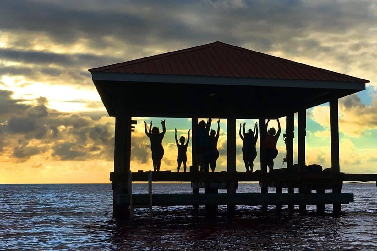 Yoga class held at Belize Yoga Retreats in an exotic hut floating overwater and looking out on the ocean horizon while teaching poses.