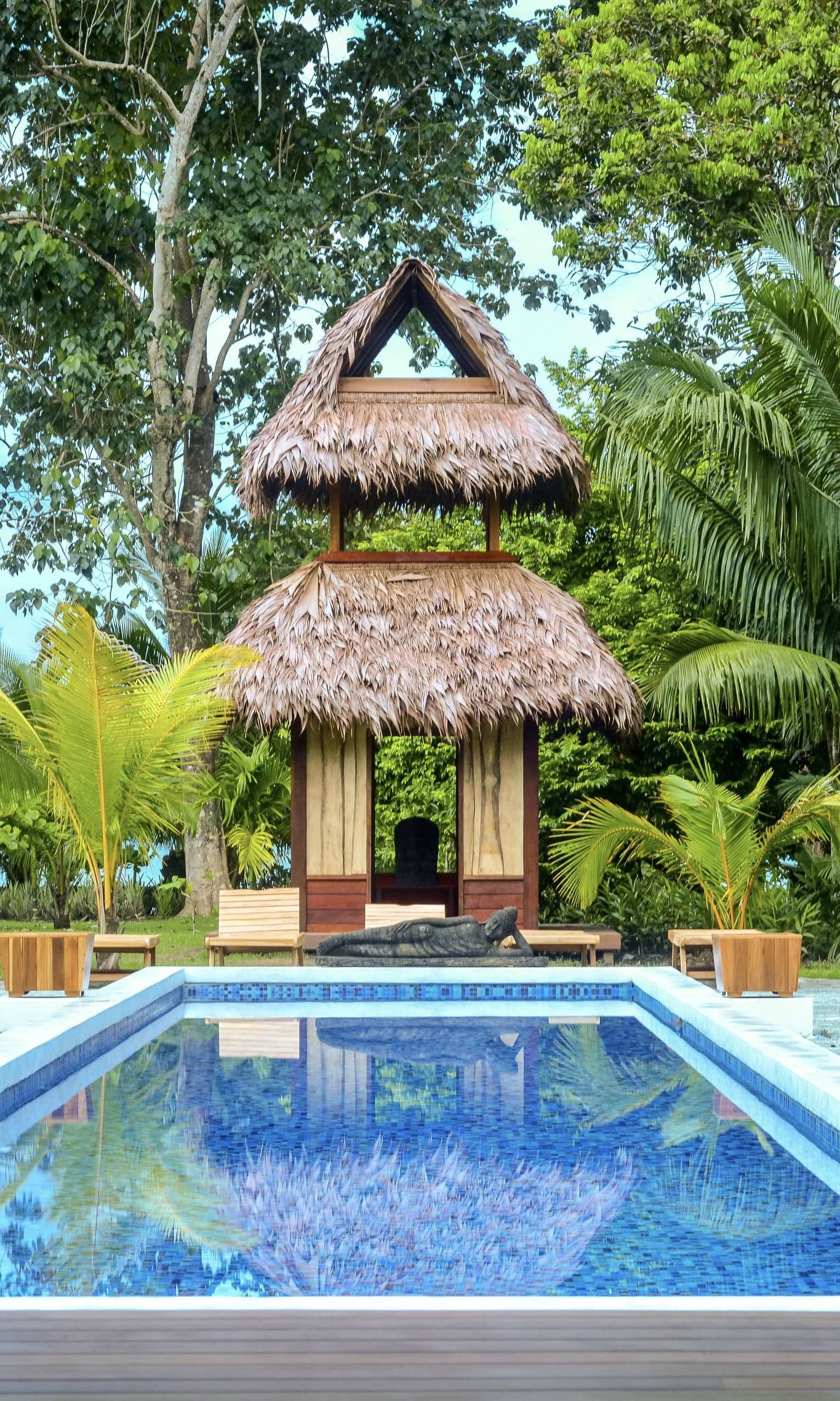 A glorious scene at the Blue Osa Yoga Retreat and Spa with bright green plants surrounding a pool and a thatch-roofed hut in Costa Rica.