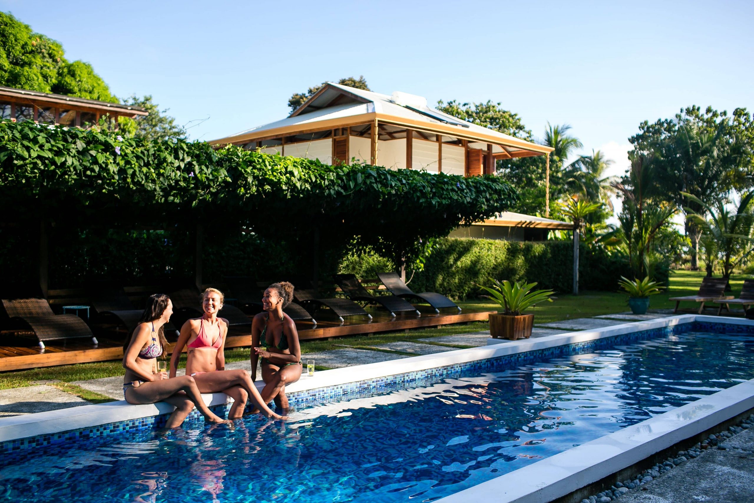 Guests enjoying the Blue Osa Yoga Retreat and Spa outside by the pool, three women sitting on the side of the pool chatting in the sun.