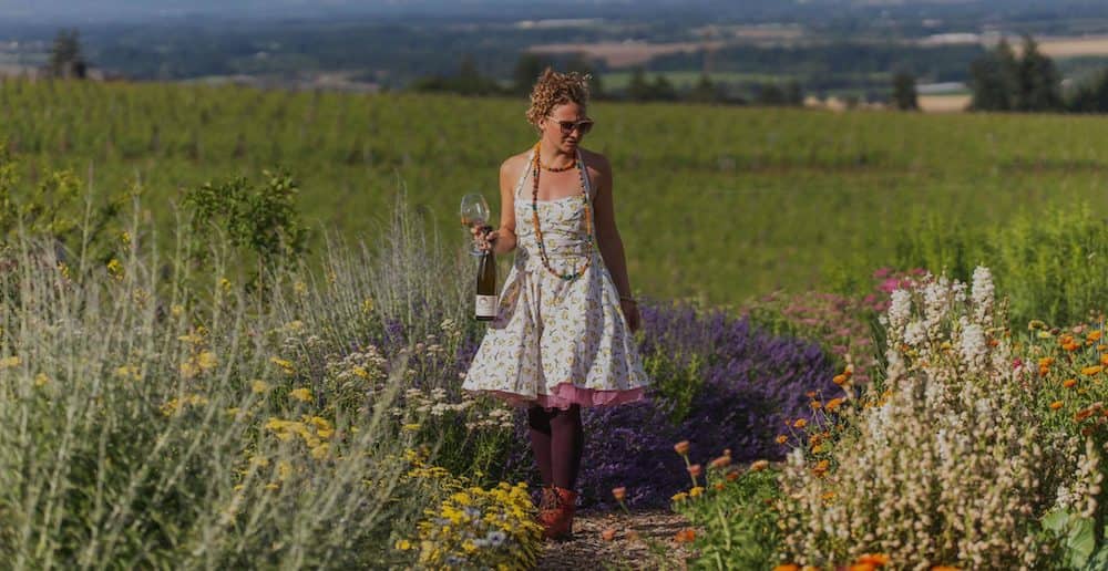 A beautiful woman in a sun dress walks through the flowers in the gardens of Brooks Wine in Oregon.