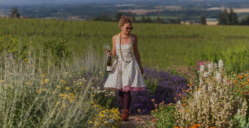 A beautiful woman in a sun dress walks through the flowers in the gardens of Brooks Wine in Oregon. 