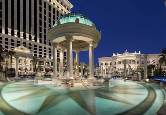 Temple Pool at Caesars Palace at night with the white columned hotel in the background.