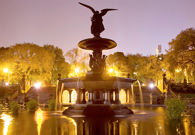 Street lamps around a fountain in Central Park at night in New York
