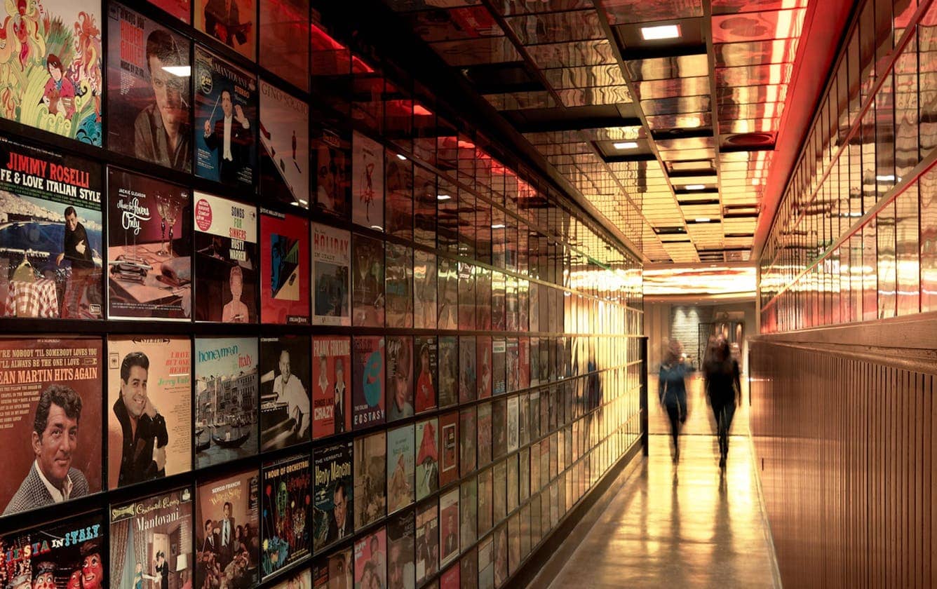 The scene at Secret Pizza inside the Cosmopolitan hotel in Las Vegas with two women walking down a hallway covered in famous album artwork and vinyl records.
