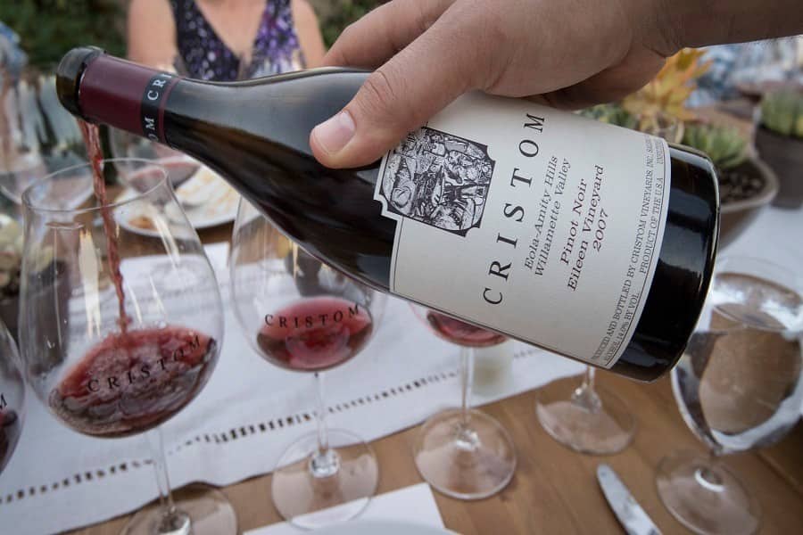 Person pouring a bottle of wine into a glass at Cristom Vineyards in Oregon. 