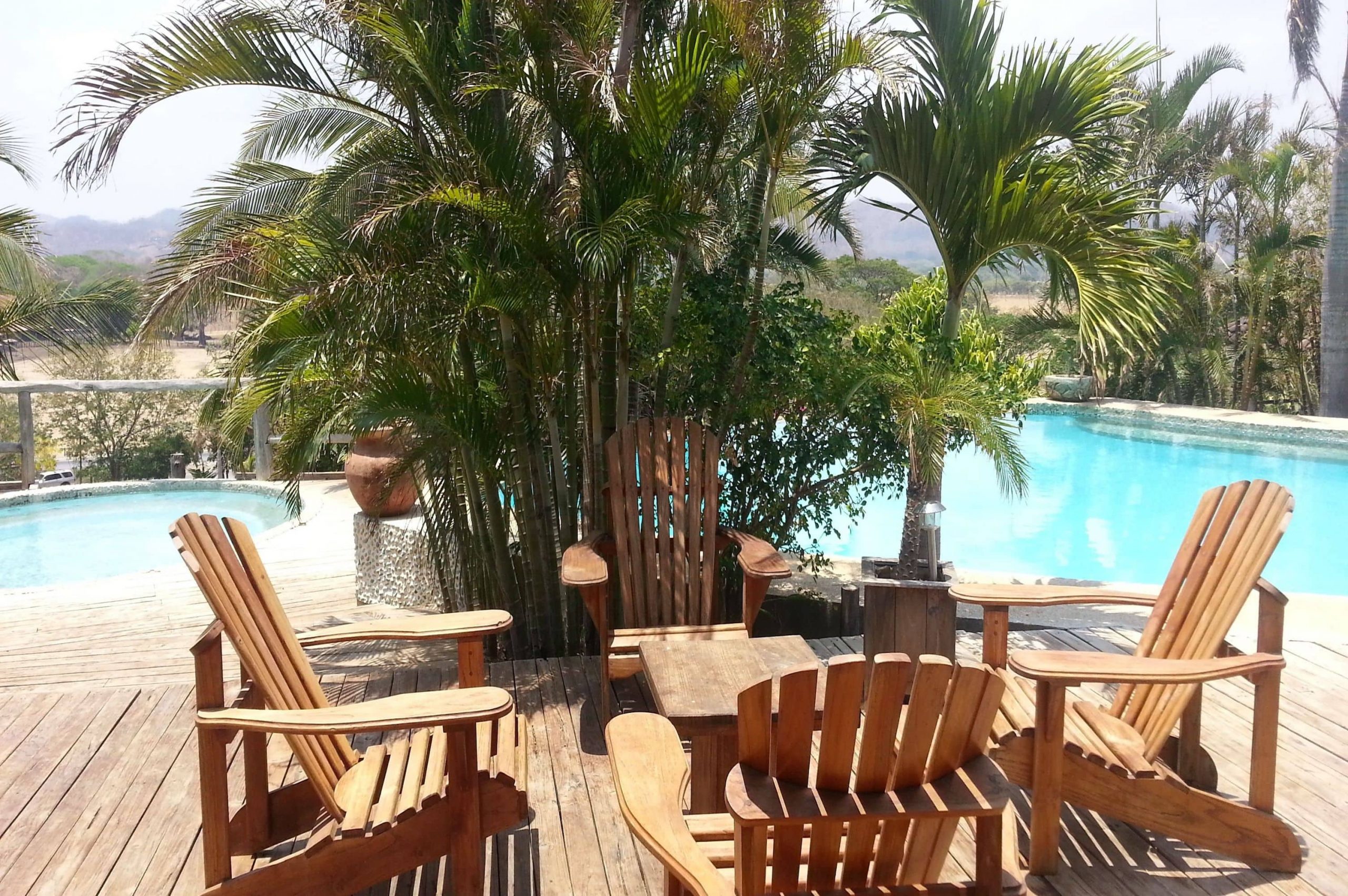 Poolside at the El-Sabanero Eco Lodge with palm trees, a pool, hot tub, and wooden deck chairs and table for sun lounging and fun.