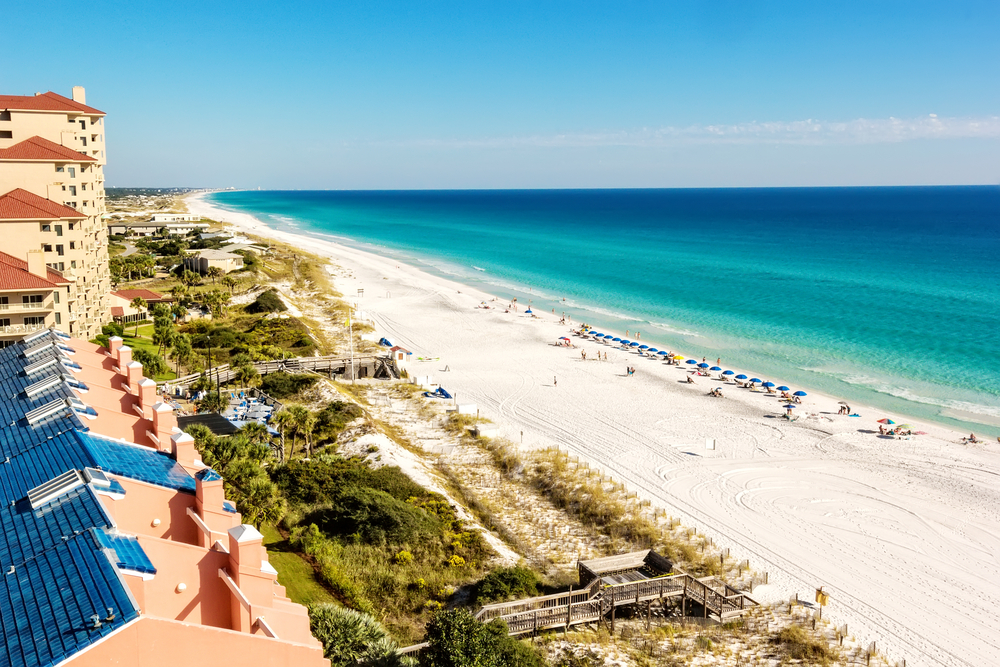 stretch of white sands beach dotted with blue umbrellas