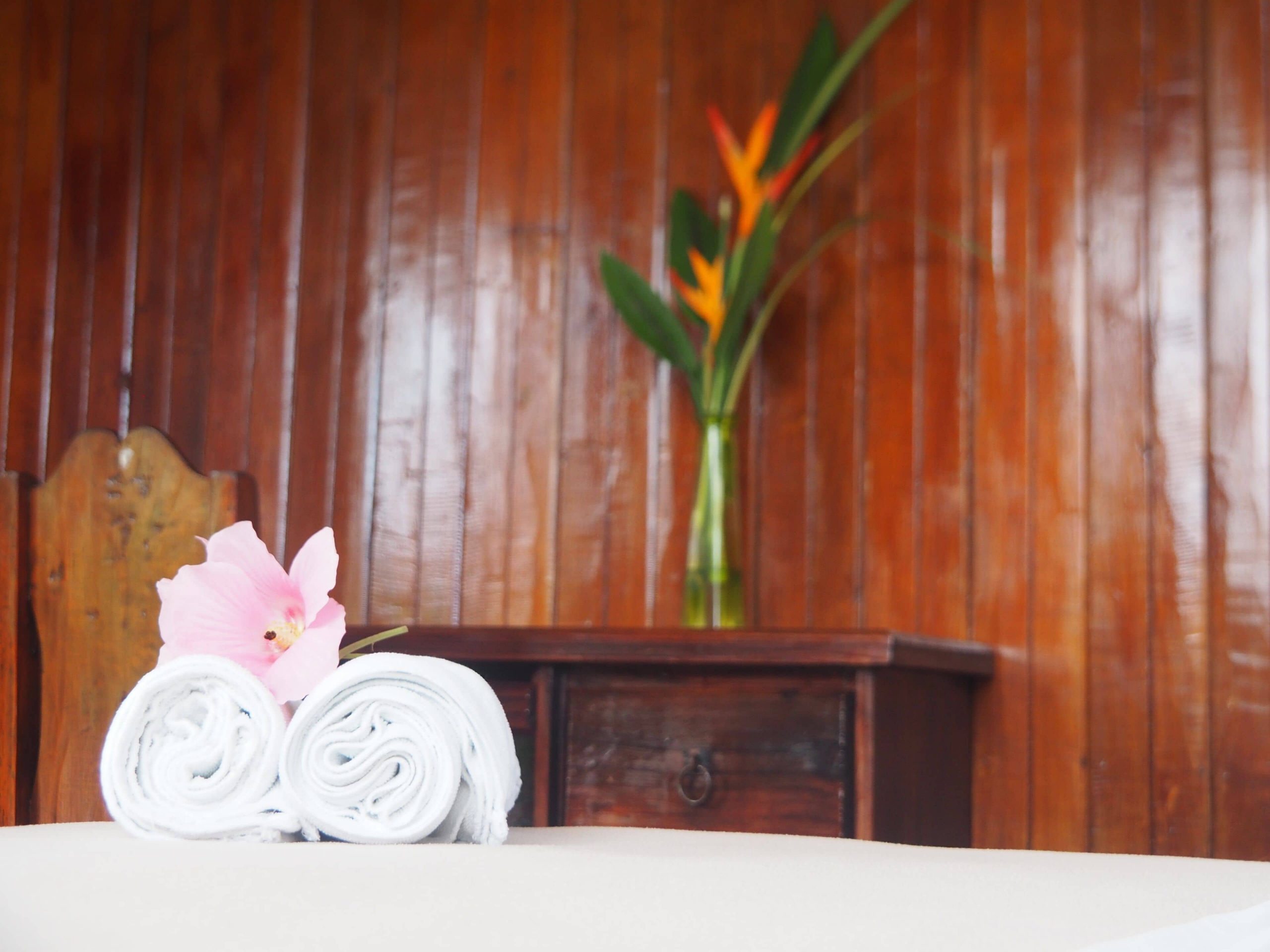 Inside one of the hotel rooms at Essence Arenal in Costa Rica features traditional wooden cabins, white linens, maid service, and colorful flowers.