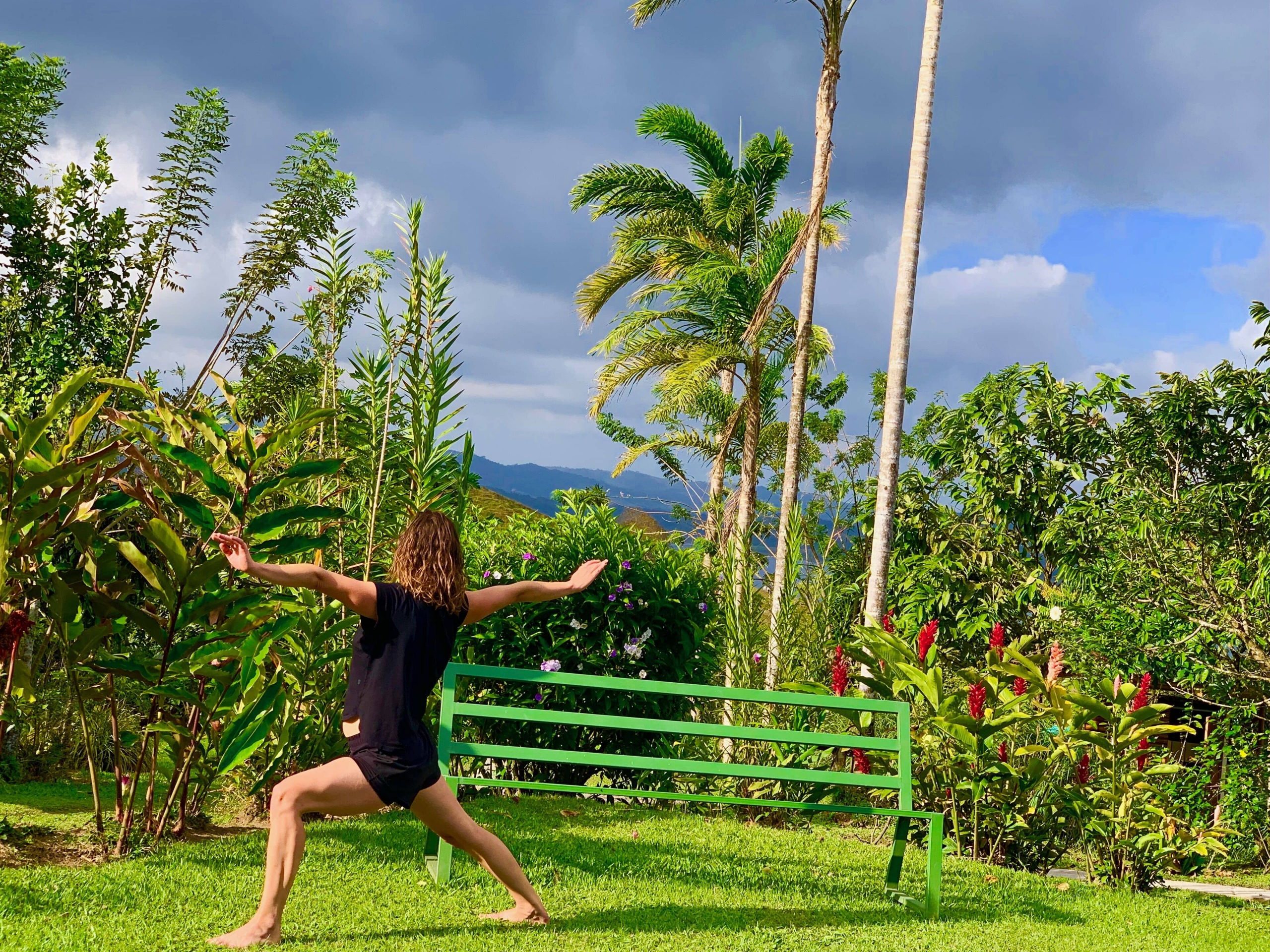 A fellow yogi at the Essence Arenal yoga retreat doing warrior pose outside in the vivid Costa Rican rainforest landscape.