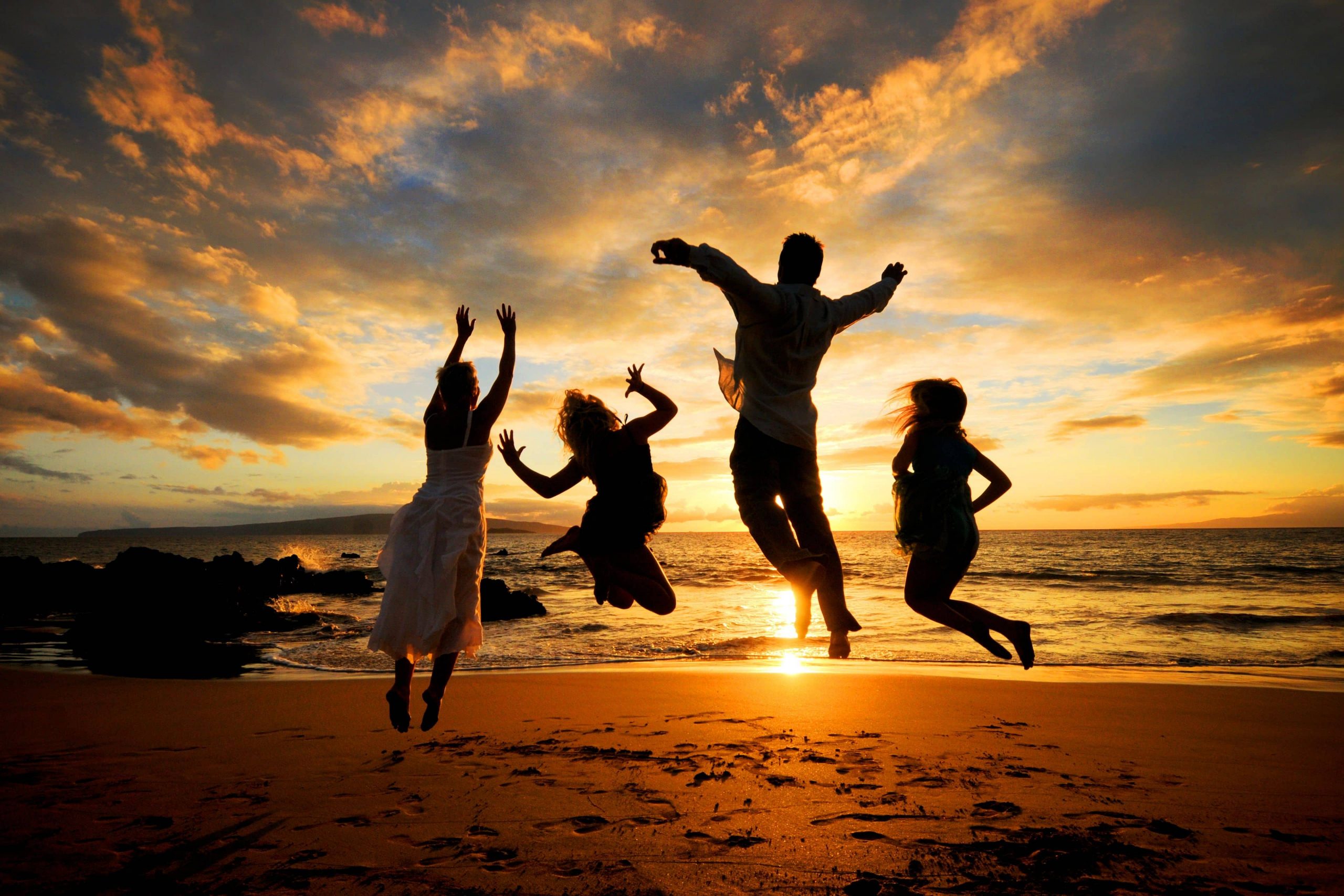 Family jumping on the beach silhouetted as the sun sets behind them over the ocean in Hawaii