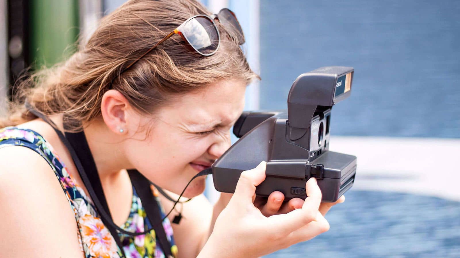 Girl squinting into the viewfinder of a Polaroid camera while taking family vacation photos