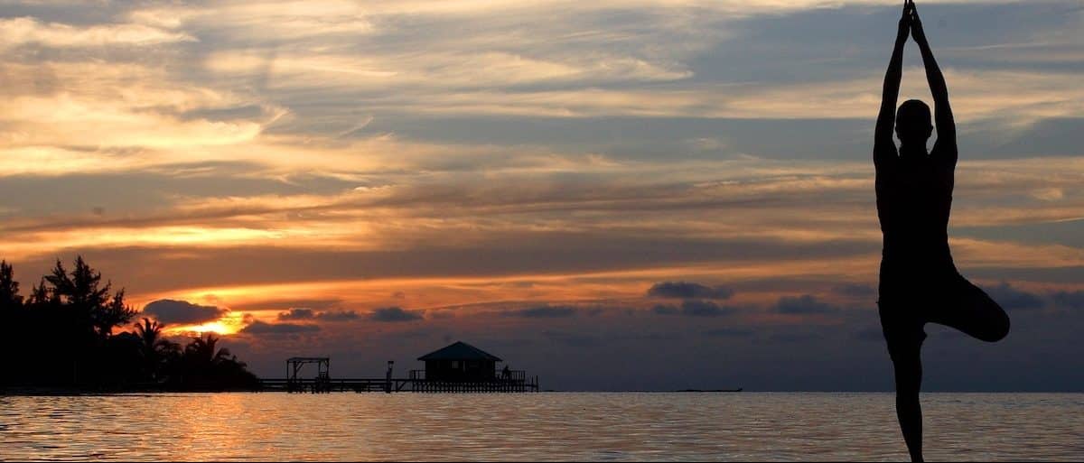 A silhouette of a woman doing yoga of a pier that looks onto a beautiful sunset at dusk during a yoga retreat run by Island Expedition Belize Adventure Basecamps, Glover’s Reef and Lighthouse Reef