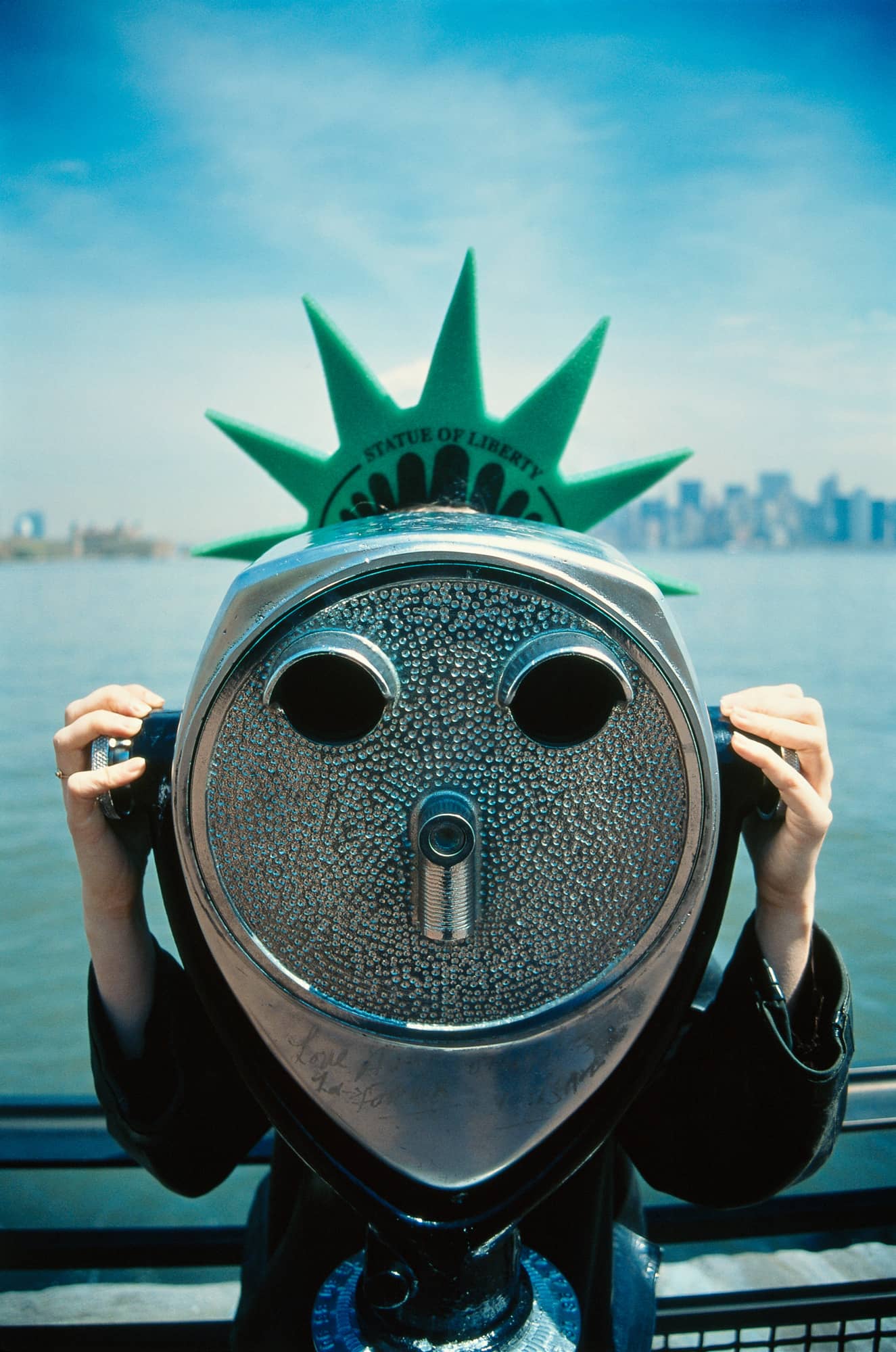 Kid wearing a statue of liberty hat looking through a viewfinder in New York