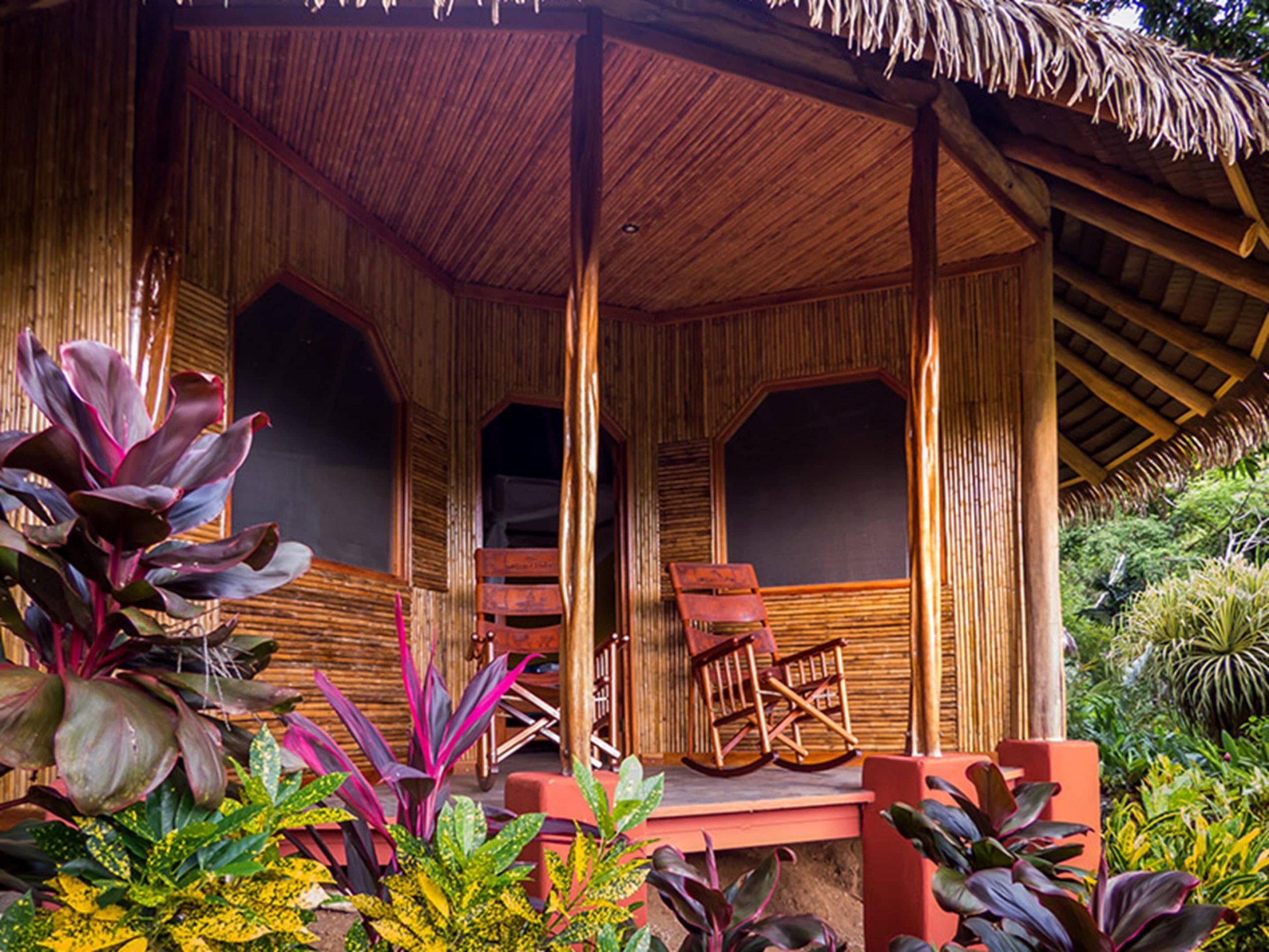 An outdoor deck with rocking chairs and colorful plants in the surrounding jungle of a private villa offered to guests of Luna Lodge in Costa Rica.
