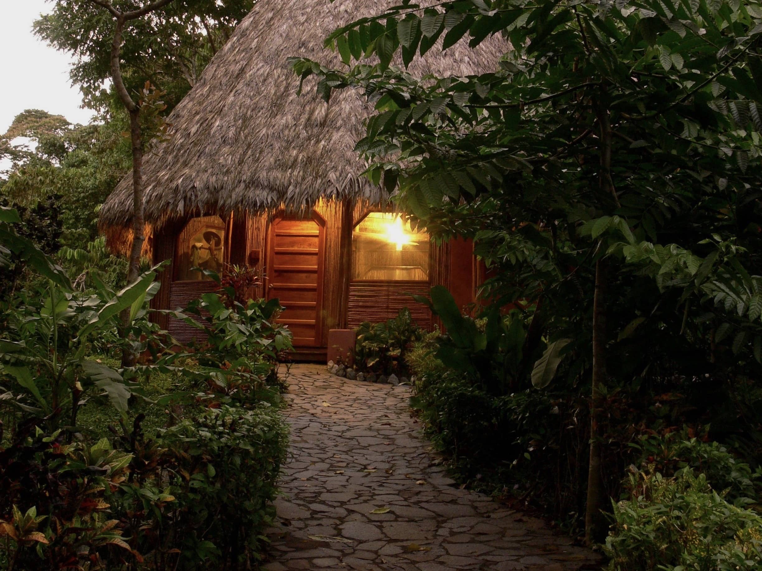 A thatch-roofed private wooden villa with stone pathway leading up to its beautiful wooden door at Luna Lodge in Costa Rica.
