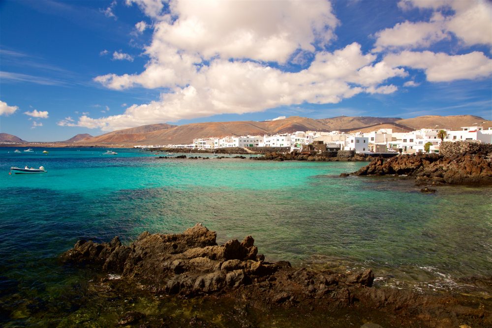 A boat cruises near the rocky shore in the clear waters of Punta Mujeres village, the Canary islands