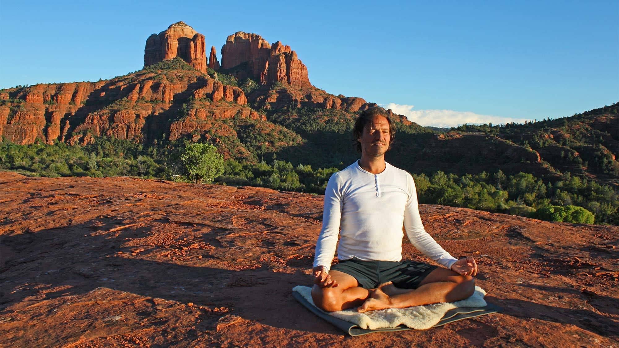 Man meditating while sitting in the red-rock desert of a Sedona Vortex