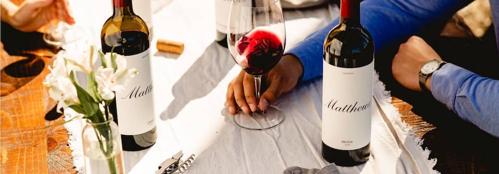 At Matthews Winery in Seattle, Washington wine country, a man is sitting at a table with two bottles of red wine and about to taste one.