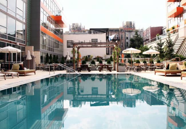 Trendy and modern pool and pool deck with city views and shrubbery at the McCarren Hotel in New York, New York.