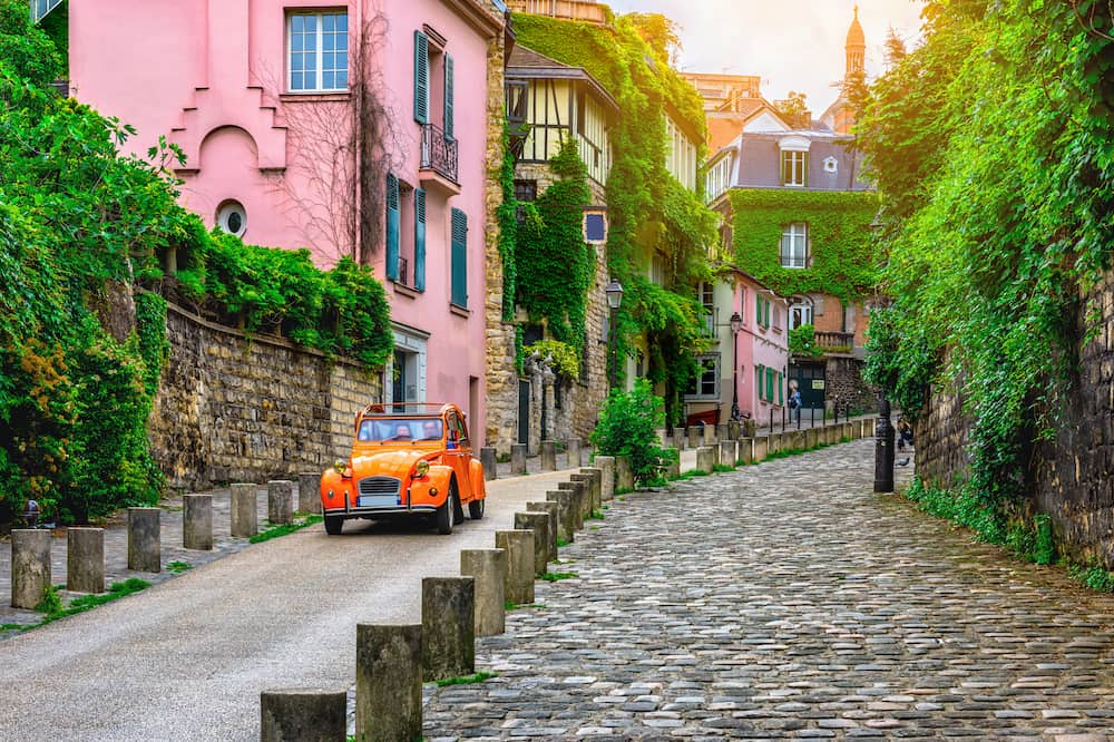 A beautiful pink home and orange car stand out on this beautiful Montmarte street in Paris, France.