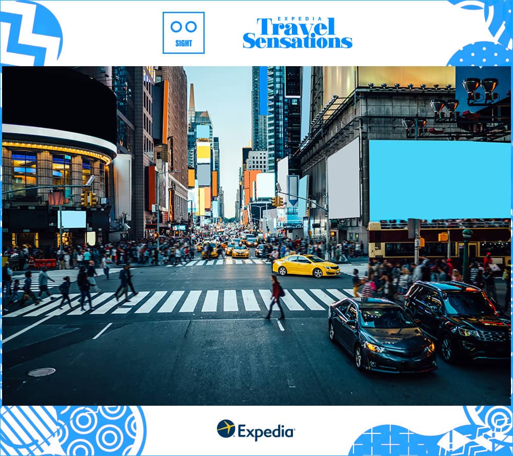 Streets of Manhattan near Times Square with yellow cabs and cars stopped as pedestrians cross at crosswalks and the billboards and sky are lit up with blues and orange tones.