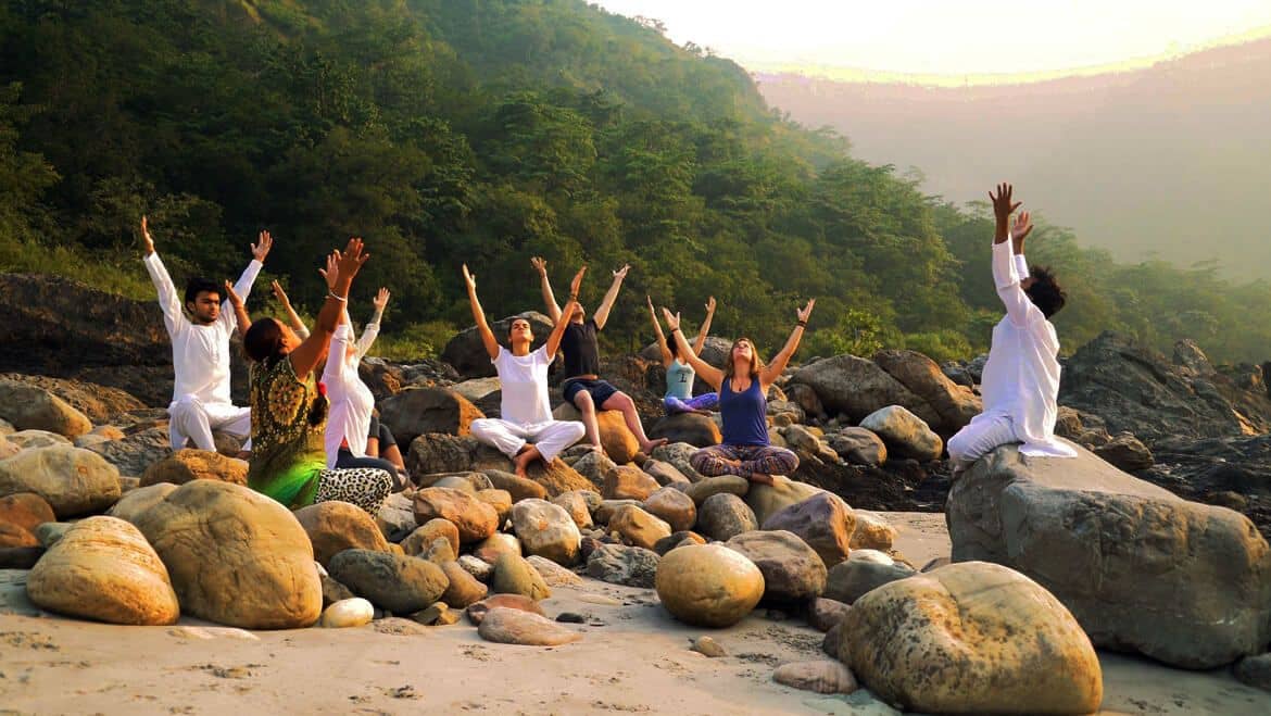 People doing yoga while sitting on large rocks on the bank of a river in India