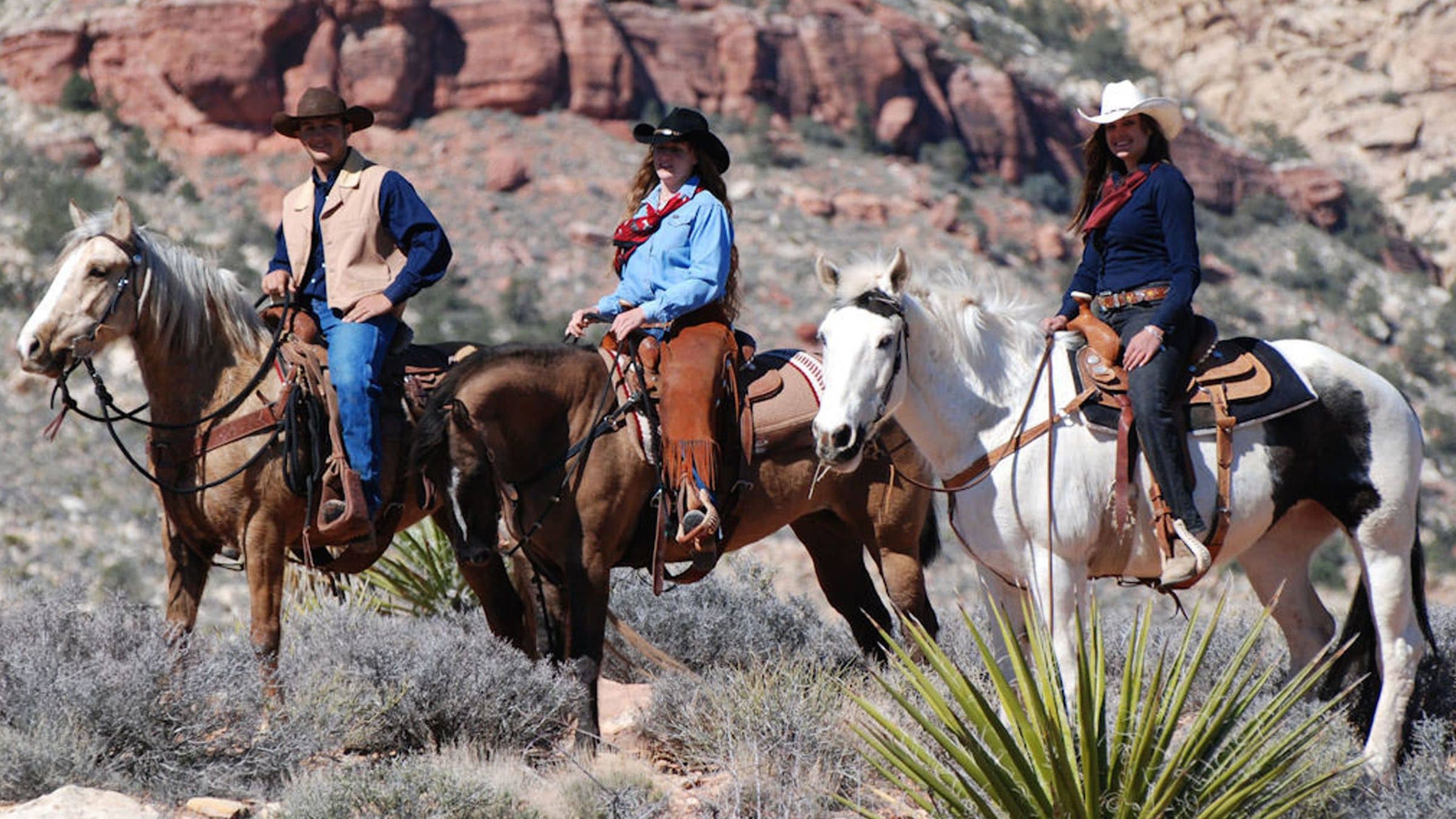 People horseback riding wearing cowboy hats in the desert near Las Vegas