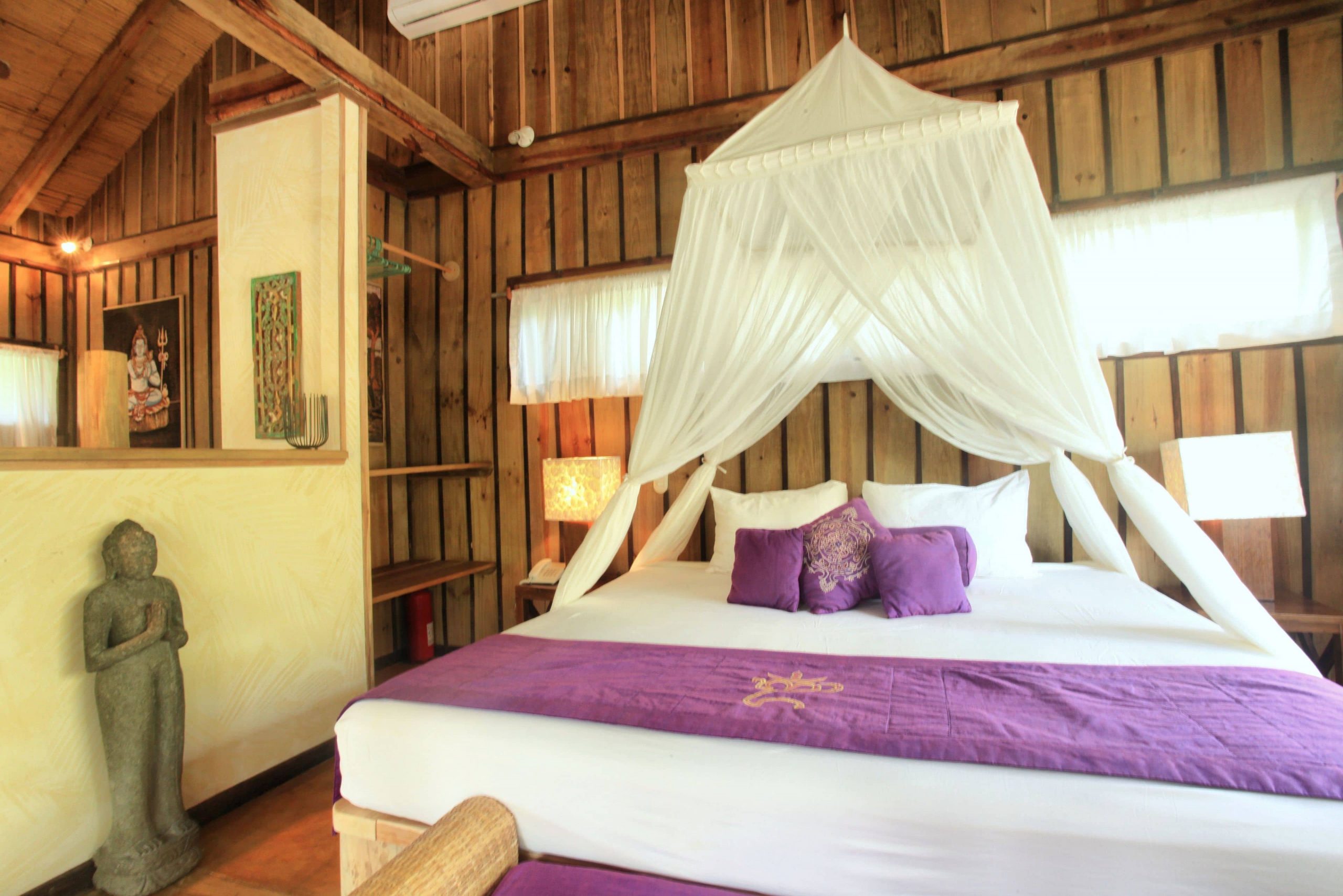 A canopy over the hotel room at the Pranamar Villas and Yoga Retreat with beautiful bed in white linens and purple decor.