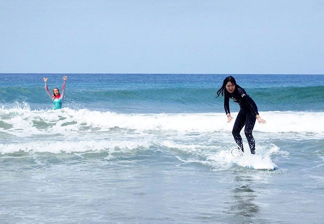 Woman surfing as instructor cheers in water in Los Angeles