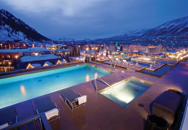 Massive pool deck and water garden at the Residences at Little Neil in Aspen at night with glowing lights of the city surrounding the pool.