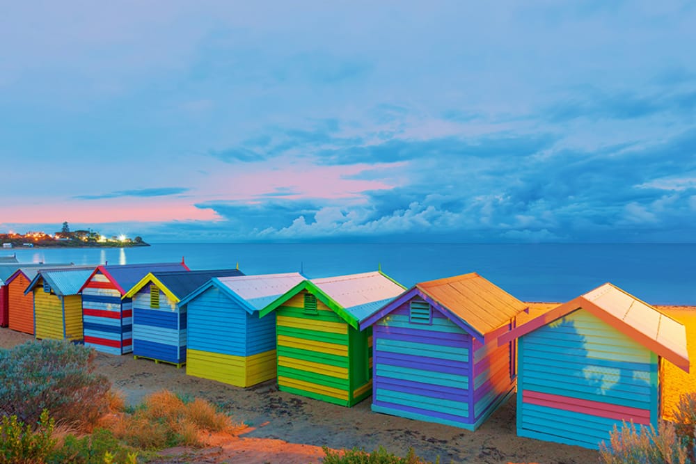 Brightly painted and designed bathing boxes standing in a row along at the sand at Brighton Beach. 