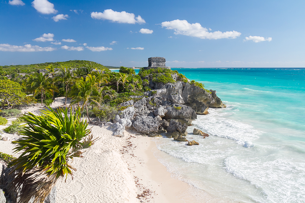 A collection of ancient ruins sitting on a cliff, overlooking the crystal clear waters of Tulum, Mexico.