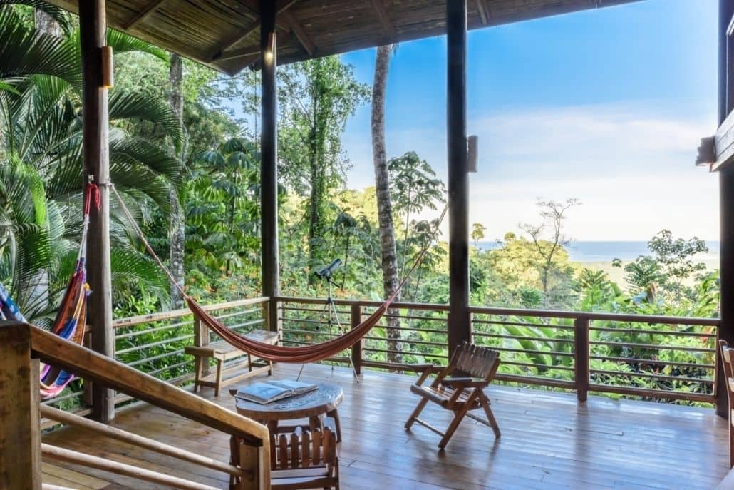 A beautiful scene in Costa Rica at the Samasati Yoga & Wellness Retreat with a large deck and hammock overlooking the rainforest canopy and clear blue ocean.