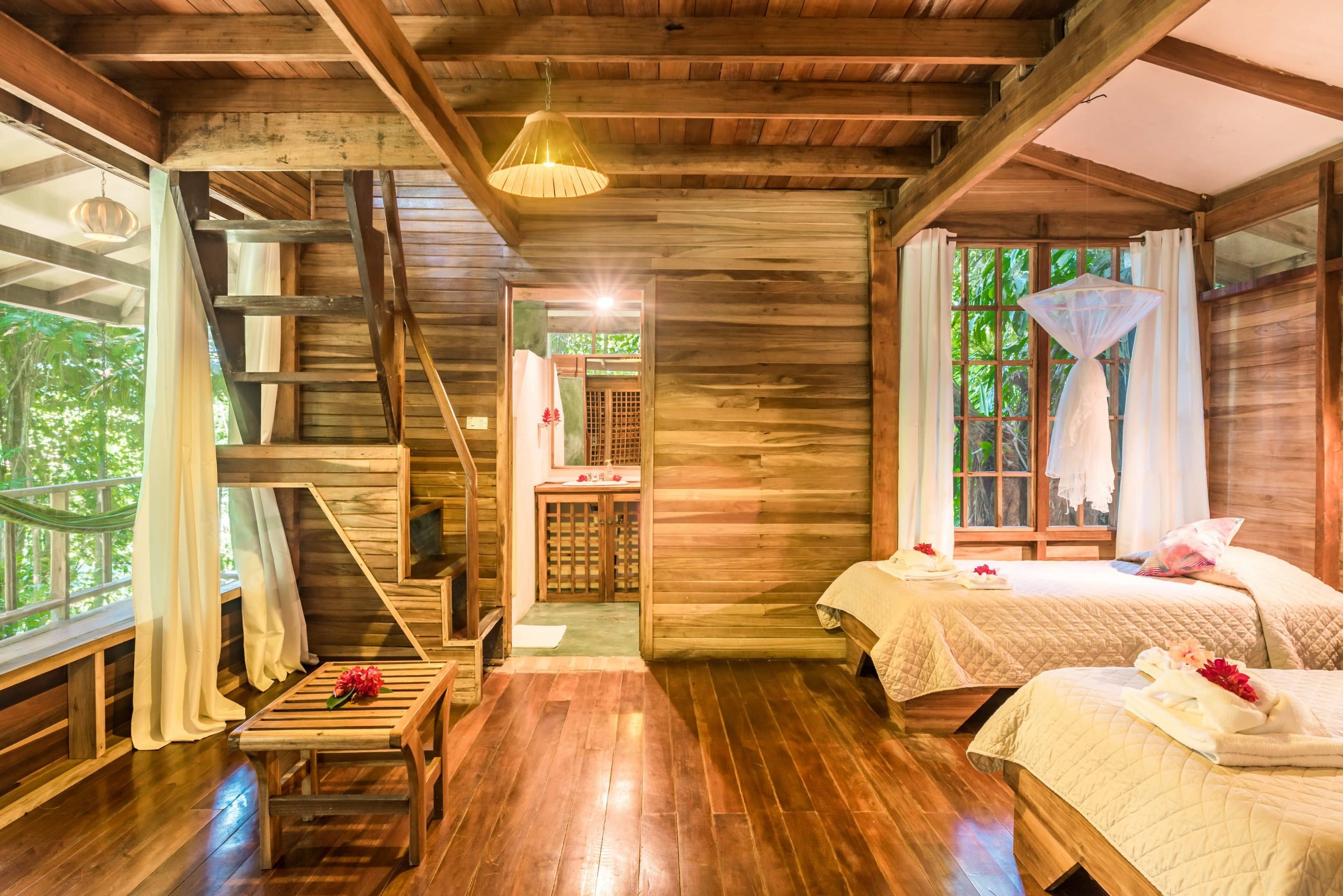 Inside one of the villas guests stay in at the Samasati Yoga & Wellness Retreat with beautiful wooden panels, white bedding, and stairs to the second floor.