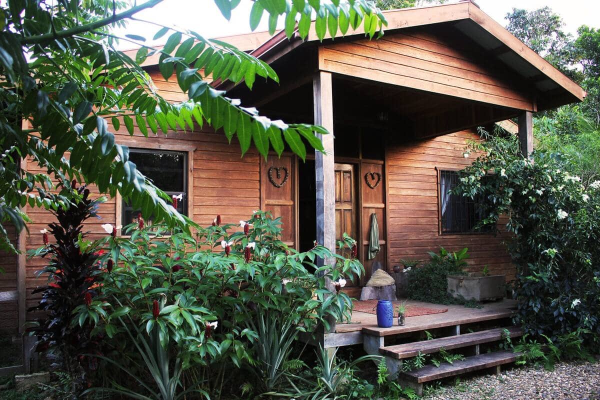 A small wooden tropical cabin with outdoor deck and surrounding by greenery at a Sattva Land, Middlesex yoga retreat in Belize.
