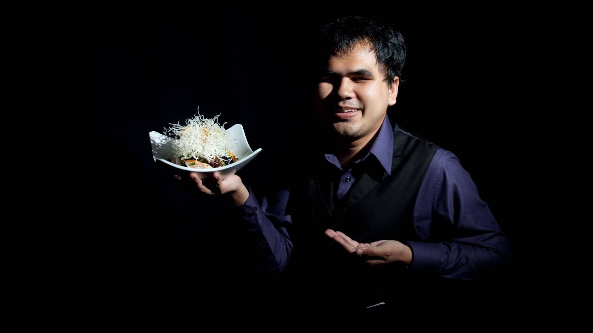 Server holding a plate of food at the dining in the dark experience in Bangkok