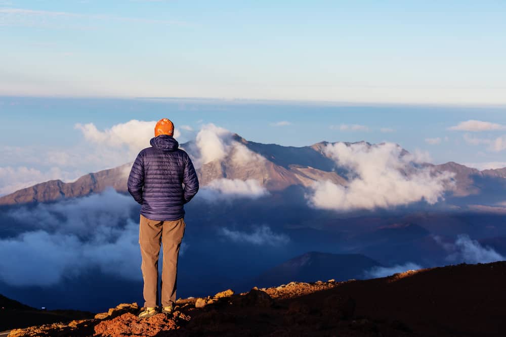 A man stands on a ridge and gazes at the Haleakala Volcano at sunrise.