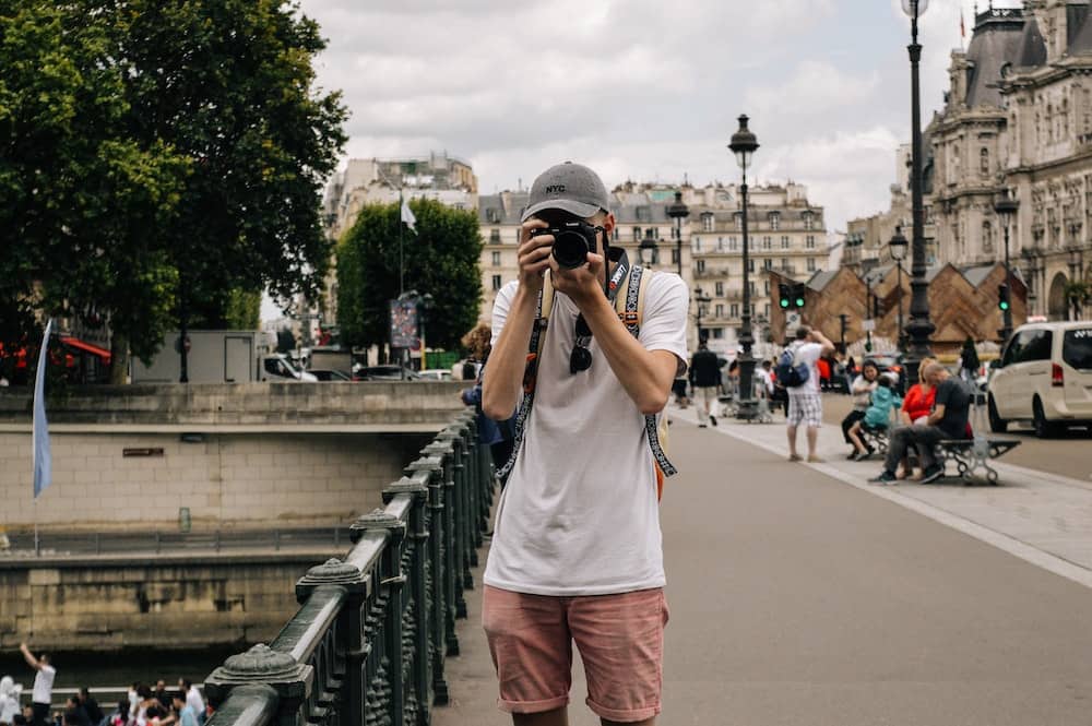 A man holding a camera in the streets of Paris taking a photo during his solo travel. 